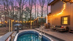 Una piscina con un deck, una zona de deck con mobiliario exterior y luces colgantes.