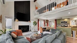 Amplia sala de estar con un sofá seccional gris grande, chimenea y una cocina equipada con electrodomésticos modernos.