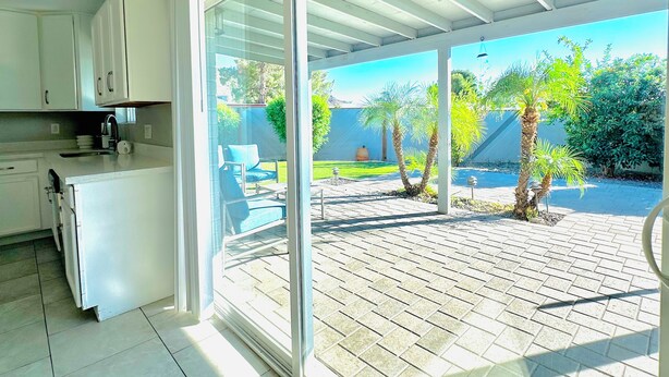 A kitchen with white cabinets, a countertop, and a sliding glass door leading to an outdoor patio with a brick floor and a small palm tree. - 3-bedroom gem in Central Phoenix (Phoenix)
