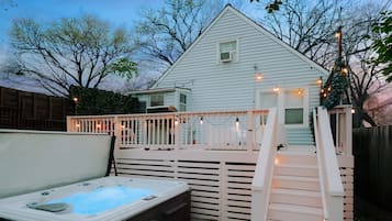 Patio trasero con jacuzzi, terraza de madera y luces colgantes.