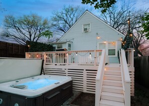 Patio trasero con jacuzzi, terraza de madera y luces colgantes.