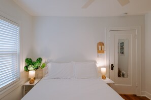 Ein Schlafzimmer mit Bett, Nachttischlampen, einer Topfpflanze und einer Tür mit Spiegel.