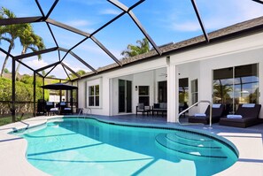 Ein Schwimmbecken mit Glasumrandung, Liegestühlen und einer überdachten Terrasse.