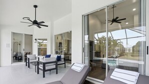 A modern spa area with two reclining chairs, a glass door leading to a pool, and ceiling fans. - 2026 Renovated Luxury Home. Heated Pool. 10 mins to 5th Ave, Pier Beach (Naples)