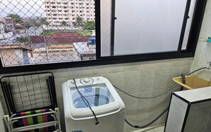 Un espace buanderie comprenant un lave-linge, un étendoir et une fenêtre donnant sur un quartier résidentiel.