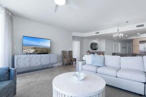 Ein modernes Wohnzimmer mit Flachbildfernseher, einem weißen Sofa, einem runden Couchtisch und einem Essbereich mit einer Chandelier.