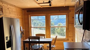 A kitchen with a wooden interior, a stainless steel refrigerator, a dining table with chairs, and a view through large windows. - Beautiful 3-bedroom barn apartment right next to Yellowstone National Park (Gardiner)