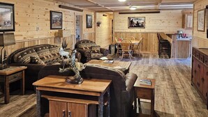 A rustic interior with a wooden ceiling, a sofa set, a dining table, and a cabinet. - Beautiful 3-bedroom barn apartment right next to Yellowstone National Park (Gardiner)