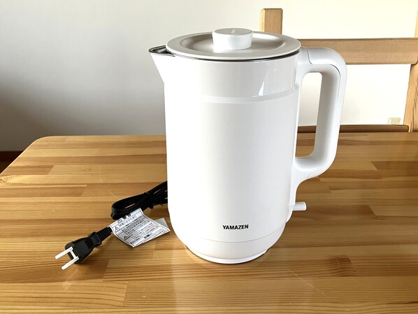 A white electric kettle with a lid and a power cord on a wooden table.