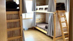 Ein Schlafraum mit Etagenbetten, einer Leiter, Holzregalen und einem Fenster.