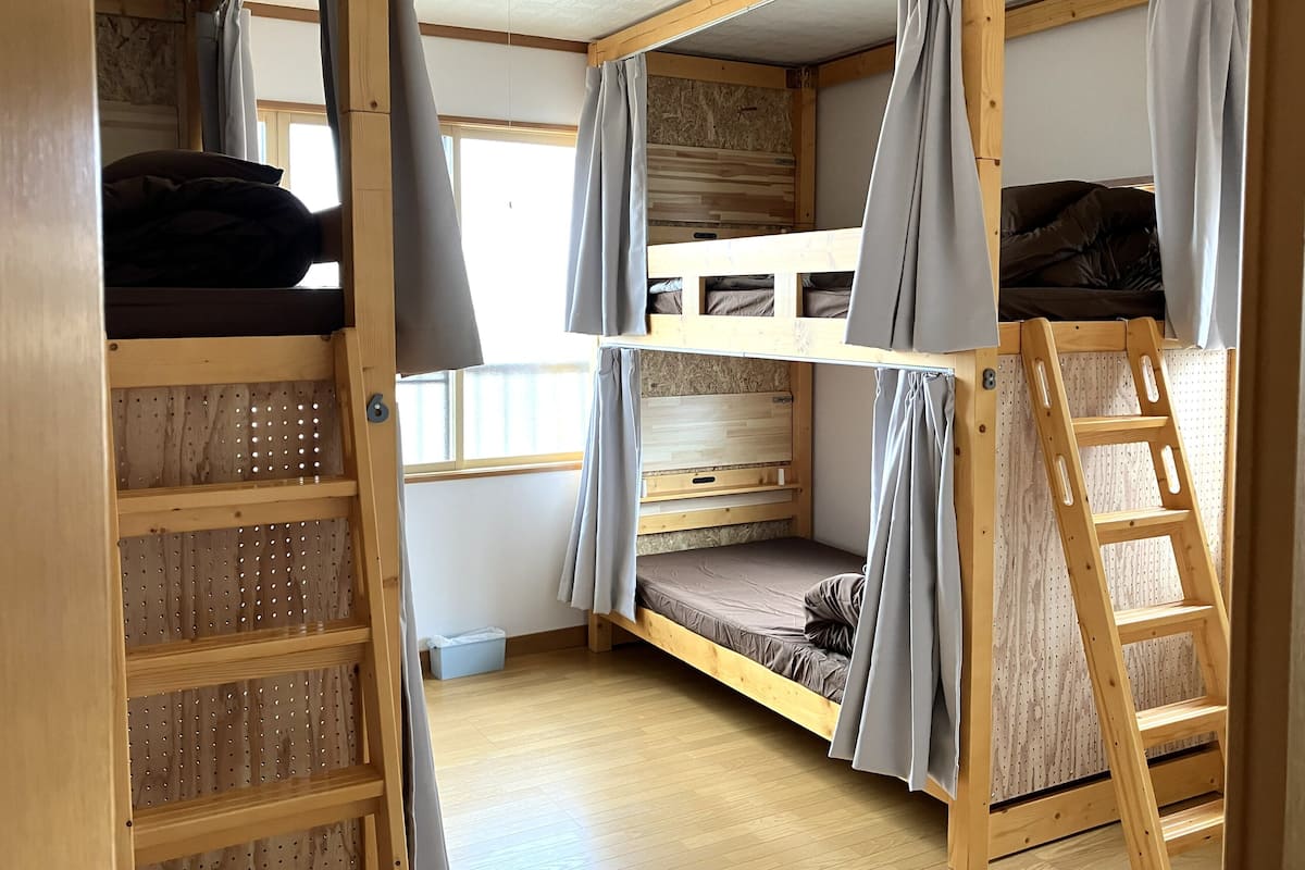 Habitación con literas, una escalera, estantes de madera y una ventana.