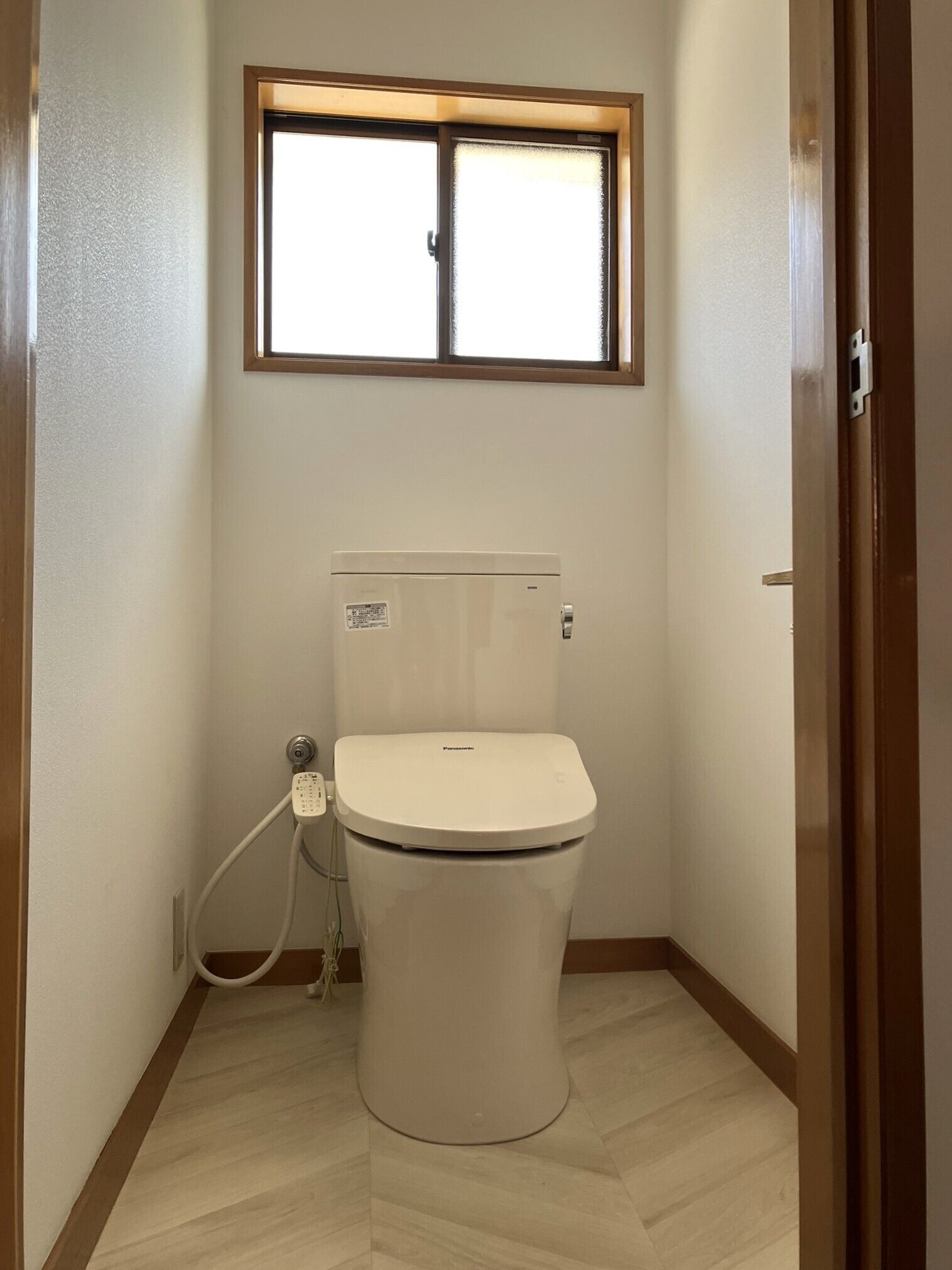 A small bathroom with a toilet, a window above it, and a wooden floor.