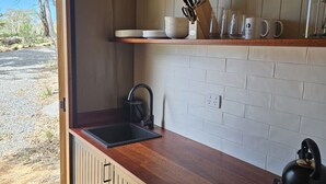 A modern kitchen with a wooden countertop, a sink, a stove, and a window overlooking a natural landscape.