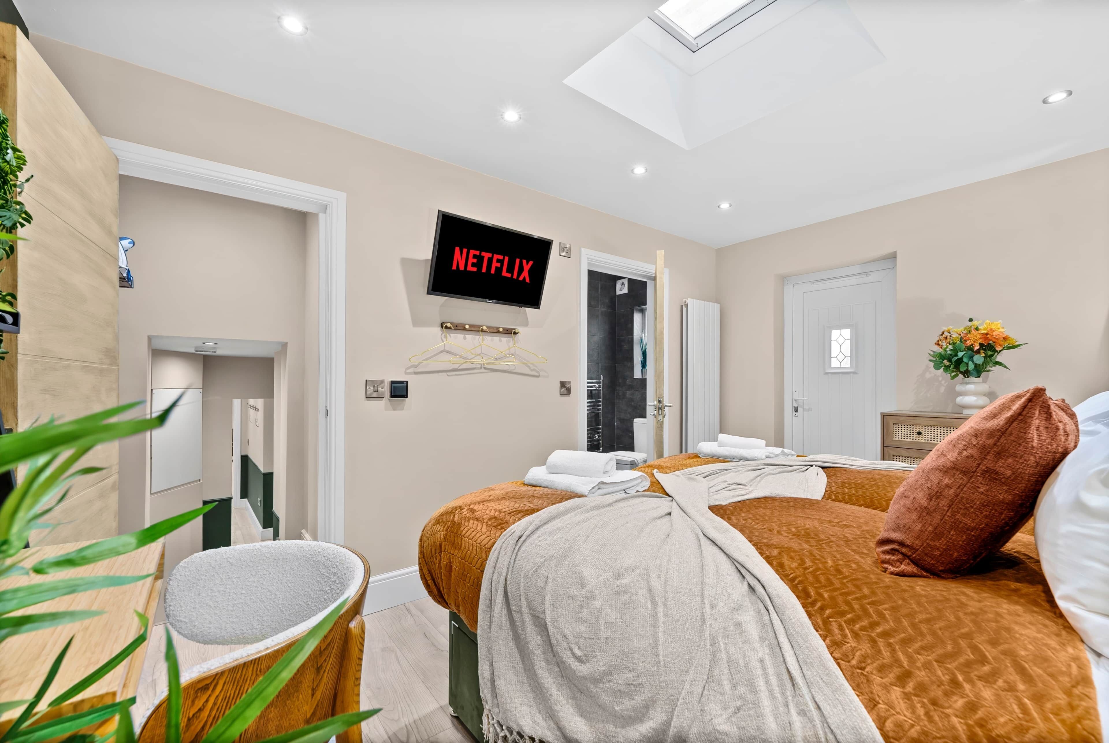 A hotel room with a bed, a TV mounted on the wall, a door, and a plant.