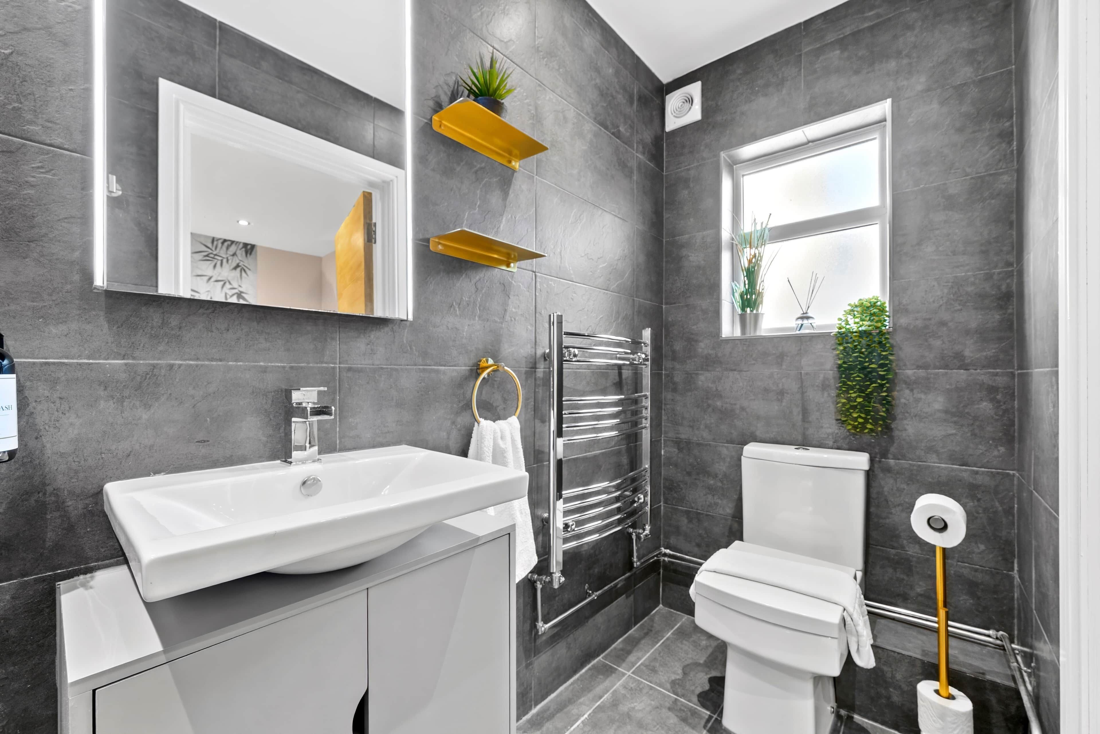 A modern bathroom with a white sink, a toilet, a towel rack, and a mirror.