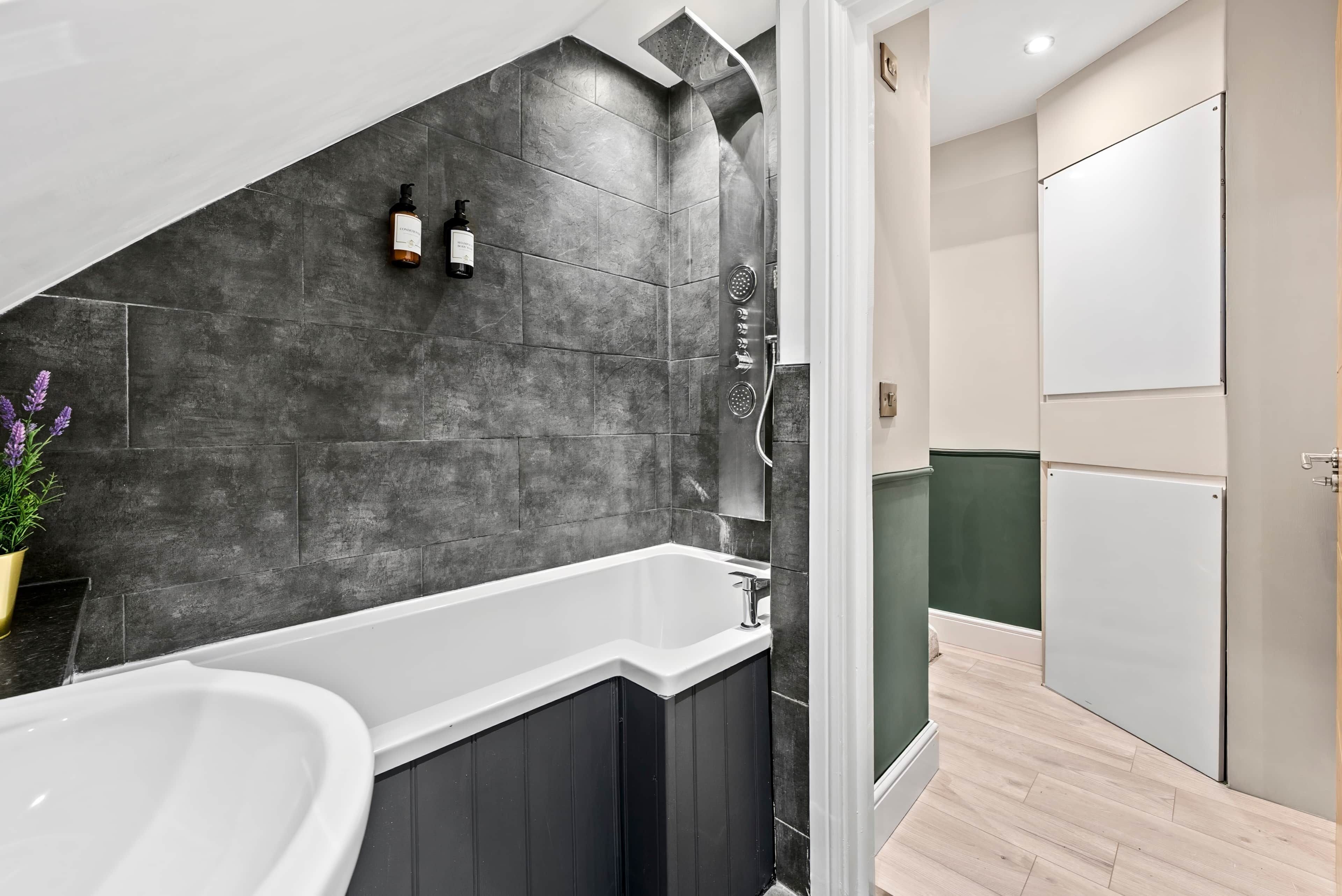 Un bagno moderno con una vasca freestanding, una doccia con soffione a pioggia e un erogatore di sapone a parete.