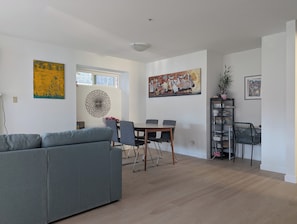 Un salon moderne avec un canapé gris, une table à manger avec des chaises et des œuvres d’art accrochées aux murs.