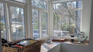 Une pièce dotée de grandes fenêtres, d’un panier en osier, d’un ventilateur et d’une boîte à motifs.