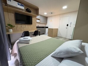 Una habitación de hotel con cama, escritorio, televisor, microondas y puerta.