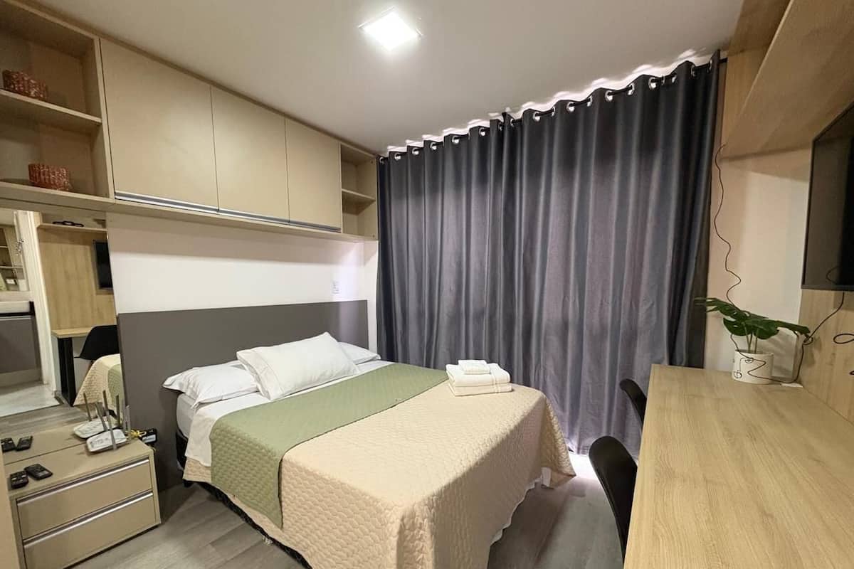A hotel room with a bed, a desk, a chair, a wardrobe, and a plant.