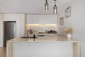 Een moderne keuken met een centraal eiland, roestvrijstalen apparatuur, hanglampen en een minimalistische inrichting.