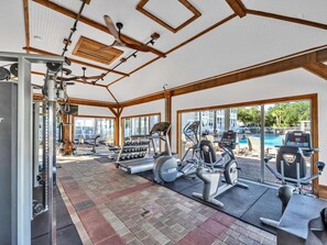 Un gimnasio con diversos equipos de ejercicio, ventanas amplias y vistas a una piscina exterior.