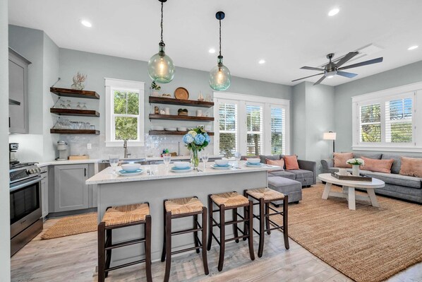 A modern kitchen with a central island, bar stools, and a ceiling fan.