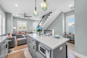 Una cocina moderna con una isla central, un comedor con sofá y una escalera.
