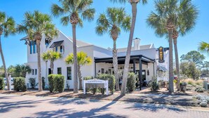 A white building with a sign 'VILLAGE PROPERTIES FOR SALE' and palm trees. - 🦩Book Me Baby! Seaglass in Santa Rosa Beach  ~ Golf Cart Included🦩 (Santa Rosa Beach)