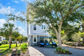 A house with a paved driveway, a golf cart, and a well-maintained garden with palm trees.