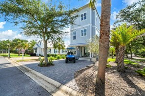 A two-story house with a paved driveway, a parked golf cart, and a well-maintained lawn with palm trees.