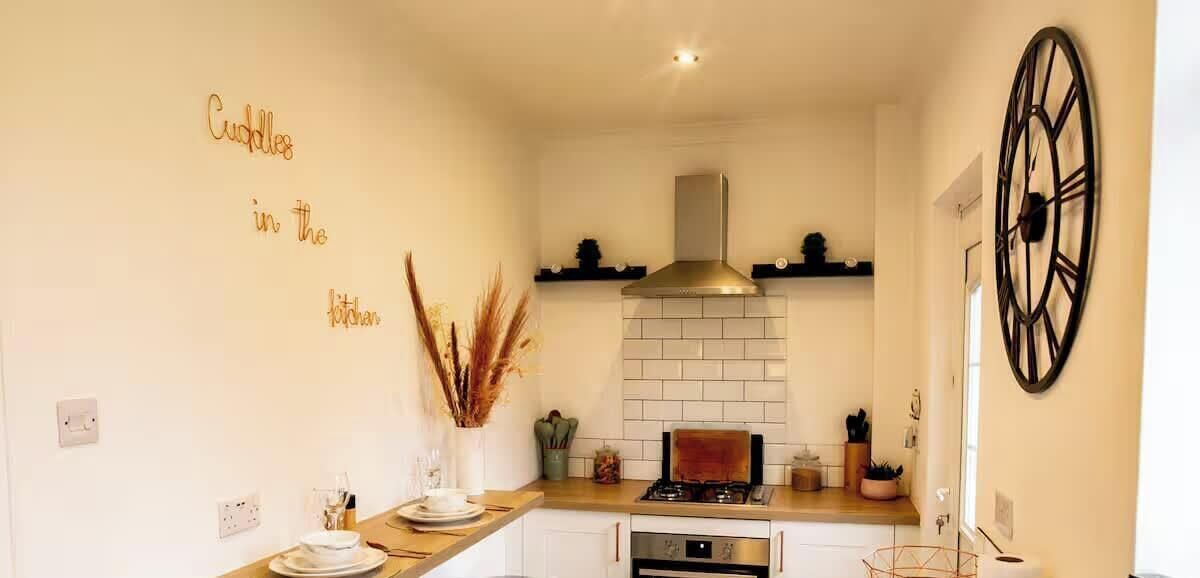 A kitchen with white cabinets, a stove, a black clock, and decorative wall text.