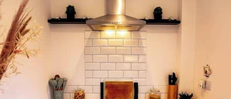 A kitchen with a stainless steel range hood, white subway tiles, a wooden cutting board, and various kitchen utensils on the counter.