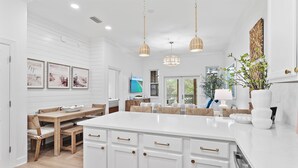 Une cuisine moderne avec des meubles blancs, un grand îlot central, des luminaires suspendus et un coin repas comprenant une table et des chaises en bois.