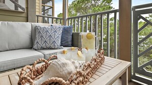 Un balcon avec un canapé, un panier en osier, une carafe de limonade et des verres.