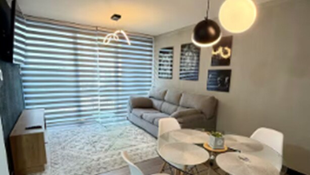 Een moderne woonkamer met een bank, een eettafel met stoelen en een hanglamp.