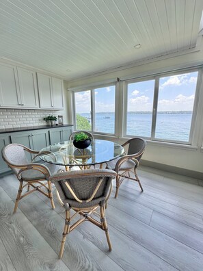 A dining area with a glass table and wicker chairs, overlooking a body of water. - The Lake House- FALL STAY-Cozy 3 Bedroom Lake Escape. Unwind by the Water! (Canandaigua)