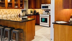 Een keuken met houten kastjes, een centraal eiland met krukken, een magnetron, een oven en een koelkast.