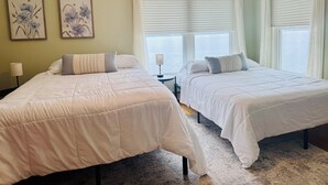 Een hotelkamer met twee bedden, een plafondventilator, een raam met jaloezieën en kunst aan de muur.