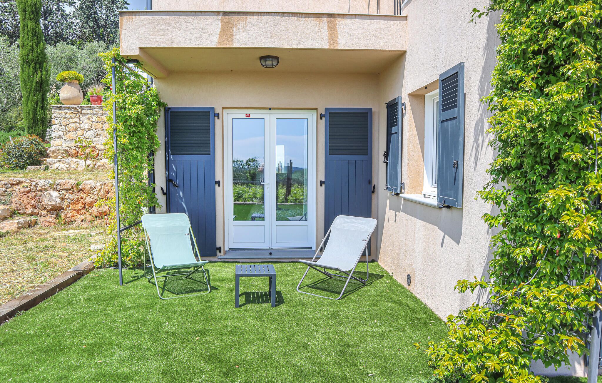 A building with a stone wall, a glass door, two lounge chairs, and a small table.