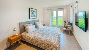 Et soveværelse med seng, natbord, stol, fjernsyn og et vindue med udsigt.