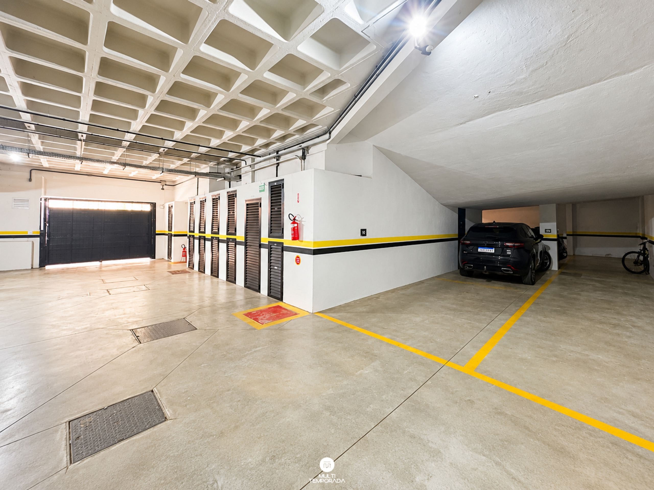 Garagem de estacionamento com vários níveis, extintores de incêndio e uma mangueira de combate a incêndio.