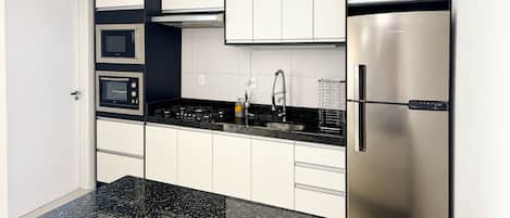 A modern kitchen with stainless steel appliances, white cabinetry, and a black granite countertop.
