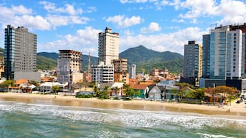 A coastal cityscape with high-rise buildings, a beach, and mountains in the background.
