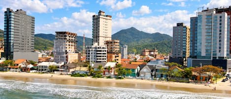 A coastal cityscape with high-rise buildings, a beach, and mountains in the background.