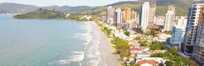 A coastal cityscape with a beachfront, high-rise buildings, and a hilly backdrop. - Apartamento Infinity Residence - PB (Porto Belo)