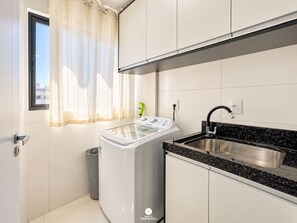 A modern kitchen with a built-in washing machine, a stainless steel sink, and a window with curtains.