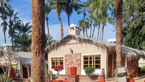 A thatched-roof building with stone walls, surrounded by palm trees and a paved courtyard. - SS 1A Cabaña rustica frente al malecón de La Paz (La Paz)