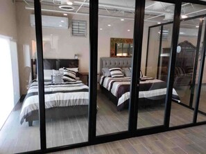 Une chambre d’hôtel avec trois lits, un grand miroir et une porte-fenêtre coulissante.