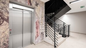 Un ascensor, una escalera con barandillas metálicas y una pared con un diseño moteado.